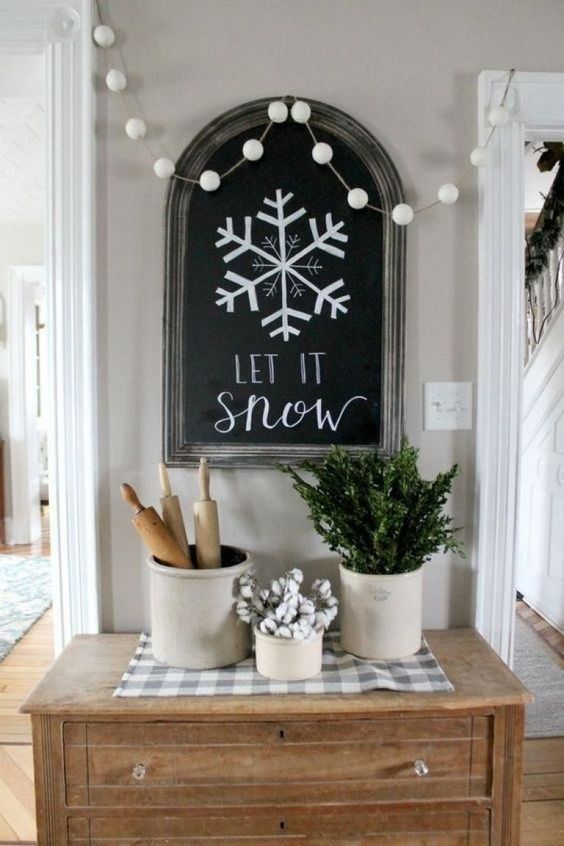 a chalkboard sign, a white pompom garland that imitates snowballs and some greenery and cotton in cans