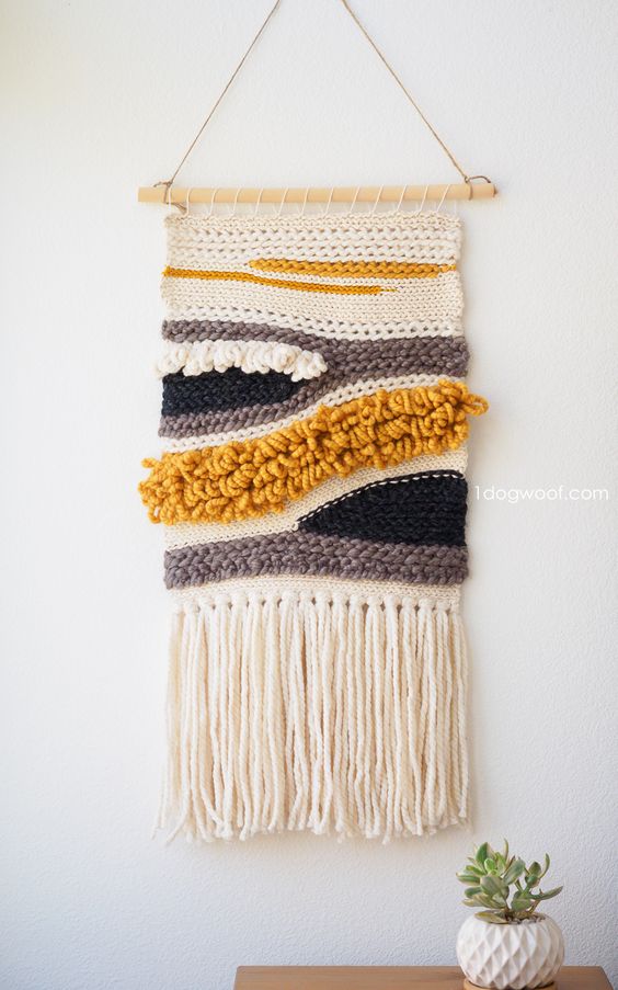 a crochet wall hanging in neutrals, mustard and black looks catchy and cool