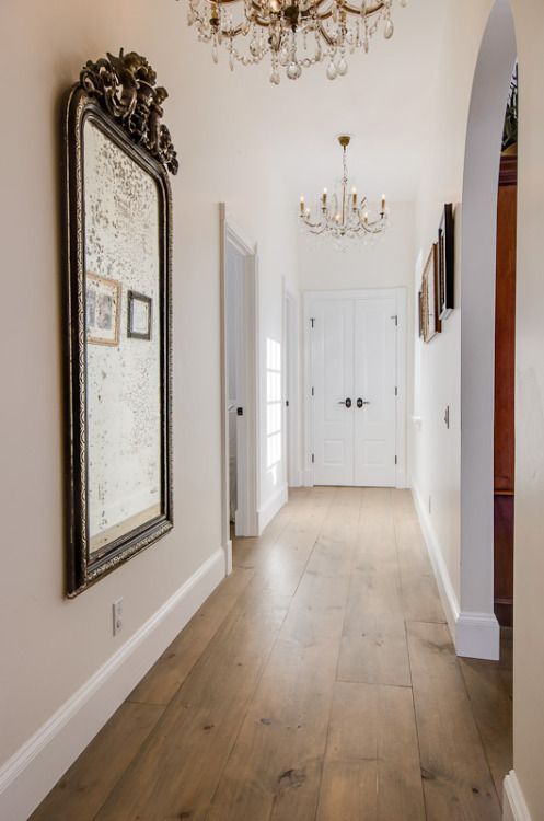 a chic entryway donen with neutral and warm hardwood floors, refined vintage mirrors and chandeliers