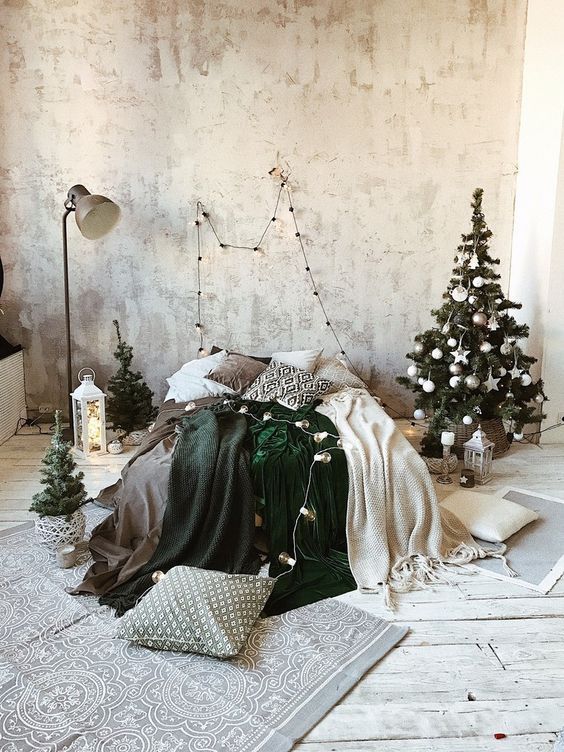 a neutral winter bedroom with a small Christmas tree decorated in white and silver, candle lanterns, green and white blankets