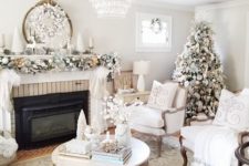 20 a refined neutral living room with a flocked Christmas tree, a garland with ornaments on the mantel and a snowy wreath