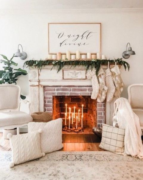 cozy winter fireplace styling with white candles, a greenery garland and candles, stockings, white pillows