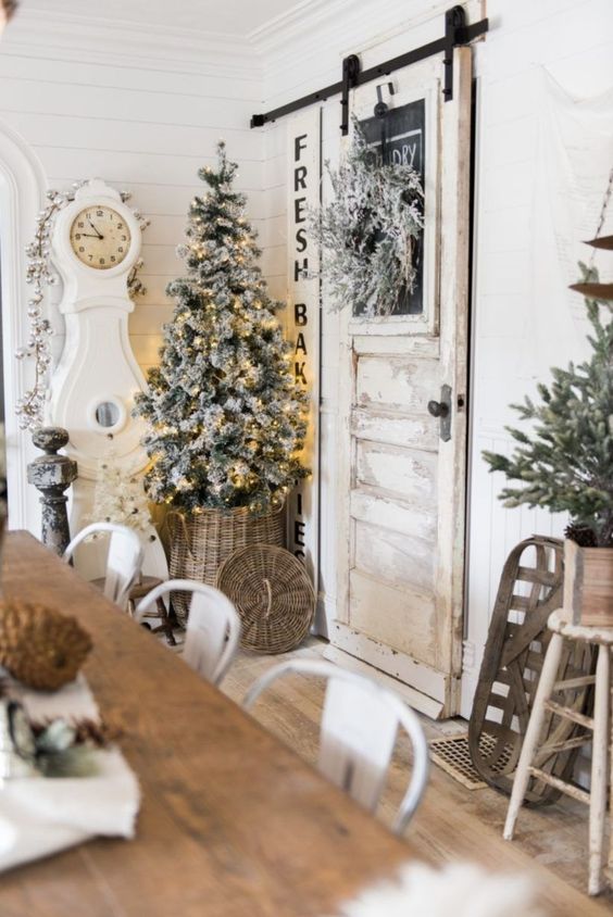 neutral farmhouse dining room decor with evergreens, a flocked Christmas tree with lights, an ornament garland and a basket