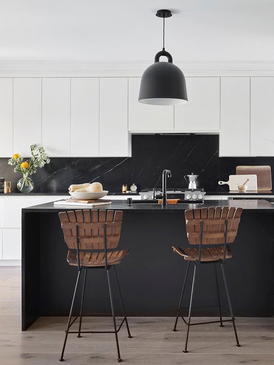 a beautiful white kitchen with sleek cabinets, a black marble backsplash and countertops, a black kitchen island, a black pendant lamp and wooden stools