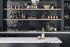 a black kitchen with a glossy black tile backsplash, open shelves, a grey kitchen island and navy stools is cool and chic
