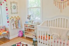 a bright and fun nursery with a colroful rug, bedding, an embroidery hoop with tassels and colorful butterflies