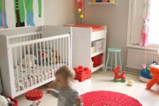 a bright and fun nursery with a whimsy artwork, colorful light garland, colorful rugs, toys and crochet baskets