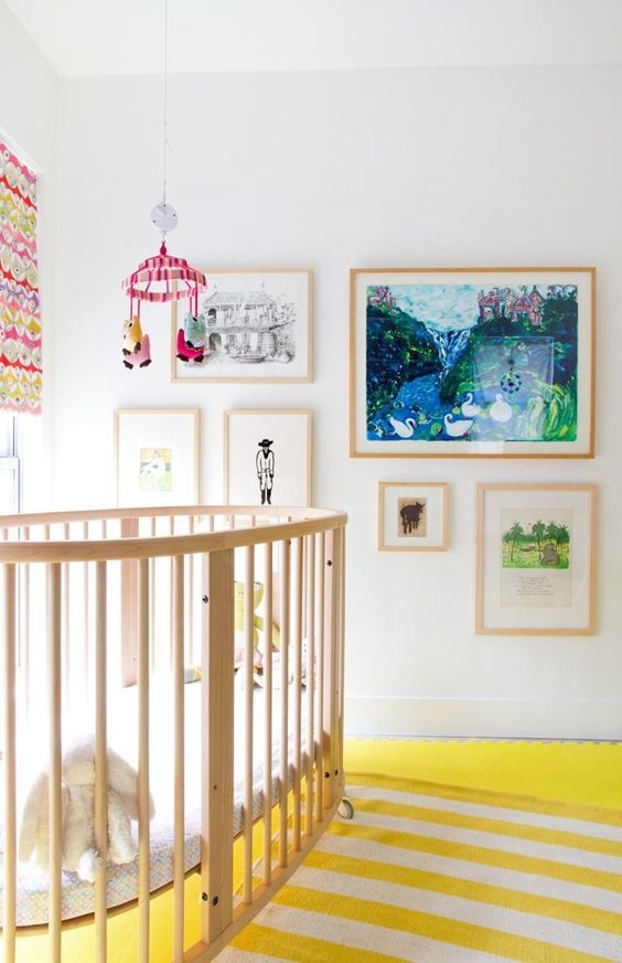 a bright and whimsy nursery with colorful layered rugs, bright artworks, a colorful mobile and curtains
