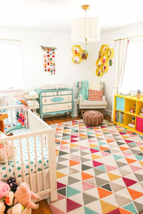 A bright mid century modern nursery with a geometric rug, colorful bedding, a mobile, a bright changing table and yellow shelves