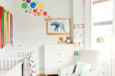 a bright modern nursery with a printed rug, a rainbow hanging, colorful bubbles and bright bedding