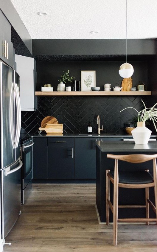 A chic black kitchen with black cabinets, a tile backsplash, concrete countertops and touches of light colored wood