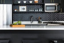 a chic black kitchen with white countertops, a black herringbone backsplash and an elegant gilded chandelier is elegant and refined