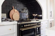 a chic vintage kitchen with white shaker cabinets, black Zellige tiles, a vintage black cooker and gold fixtures and touches