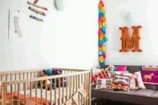a colorful boho nursery with a bright rug, colorful tassel garlands, a mobile and bright textiles all over