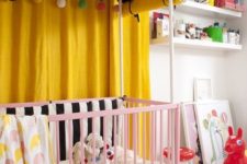 a colorful nursery with yellow curtains, a pink crib, a printed rug, colorful accessories and lots of toys