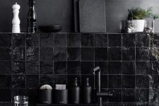 a dramatic black kitchen with black quartz countertops, a black glossy tile backsplash and a matte black wall is very cool