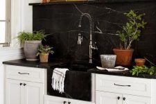 a farmhouse kitchen in white is spruced up and made more eye-catchy with a black marble backsplash and countertops