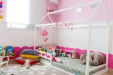 a fun nursery with pink walls, colorful bedding and a fun rug, colorful toys and artworks is amazing space