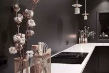 a moody black kitchen with black walls, glossy cabinets, white countertops and white pendant lamps is a stylish idea