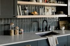 a moody farmhouse kitchen with navy cabinets, white countertops, a grey skinny tile backsplash and open shelves