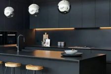 a refined minimalist black kitchen with sleek cabinets, a matte backsplash and countertops, tall stained stools and polished metal pendant lamps
