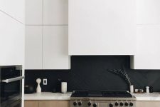 a stylish minimalist kitchen with light stained cabinets, white upper ones, a matte black herringbone backsplash and white quartz countertops
