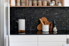 a stylish modern kitchen with sleek white cabinets, a black stacked tile backsplash and black countertops, box shelves
