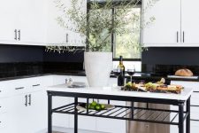 a stylish white kitchen with glossy black tiles and a chalkboard backsplash, a black and white kitchen island is very chic