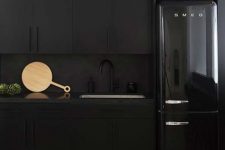 a total black kitchen with matte cabinets, a matte backsplash and a shiny and glossy fridge is a bold idea