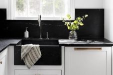 a white farmhouse kitchen with black quartz countertops and a matching backsplash plus mismatching metals for fxitures
