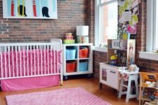 pink bedding, a pink rug, colorful artworks make this nursery with brick walls very whimsy and very bold
