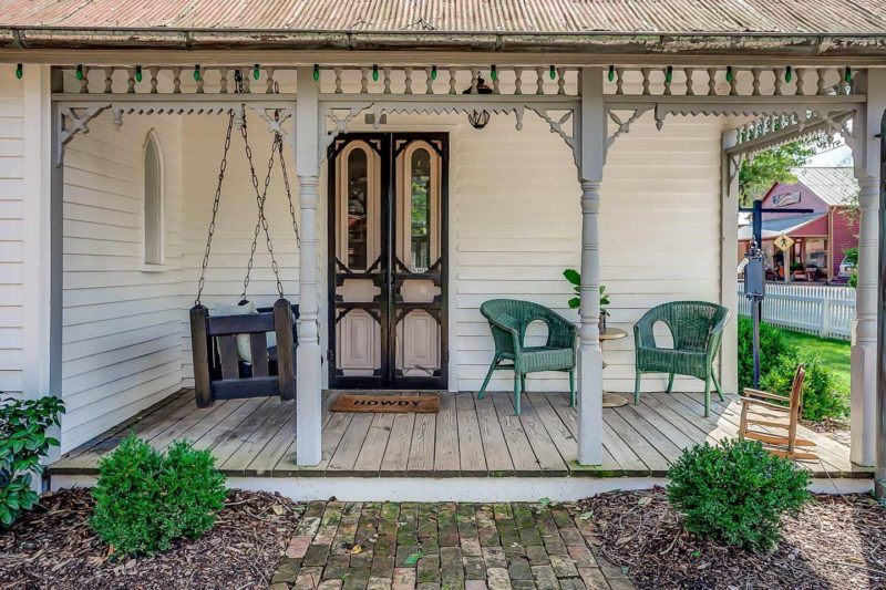 The porch features original black and pink doors, there's a hanging daybed and a green woven chair for a cozy feel