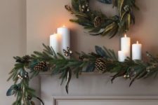 02 a chic evergreen garland with gilded touches, pinecones and a matching wreath over the mantel plus pillar candles