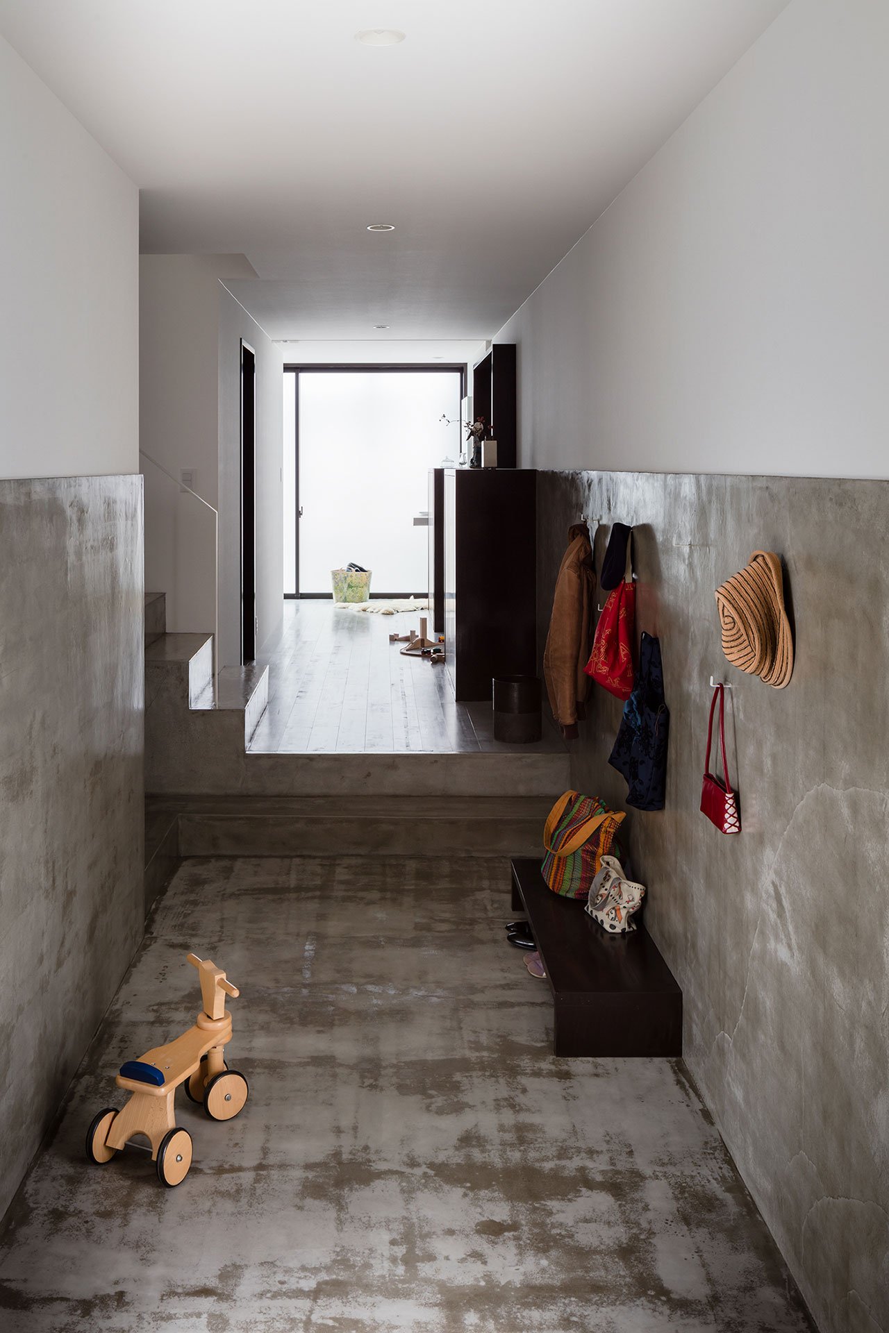 The entryway is done with concrete, a wooden bench and some hooks on the walls