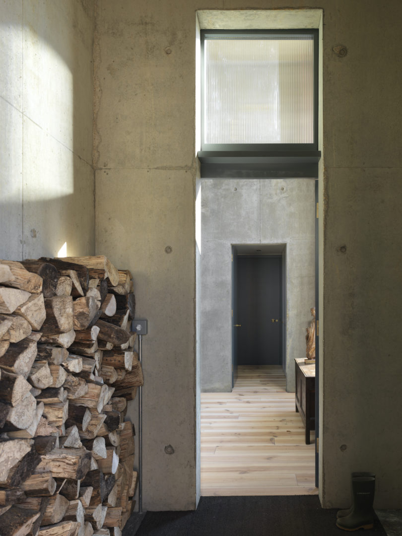 The house is done with raw concrete inside and wooden floors, and there's a firewood storage in the entrance