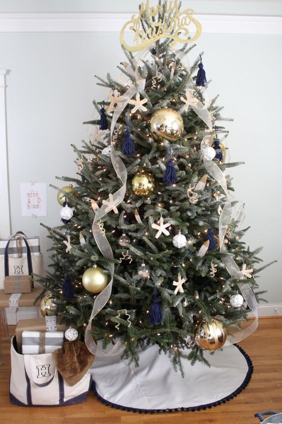 a chic beach Christmas tree with lights, navy tassels, starfish ornaments, oversized metallic ones and ribbons and a calligraphy topper