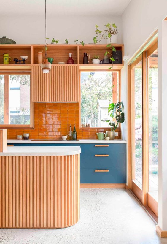 A warm colored and wood slab clad kitchen with some classic blue cabinets with wooden handles