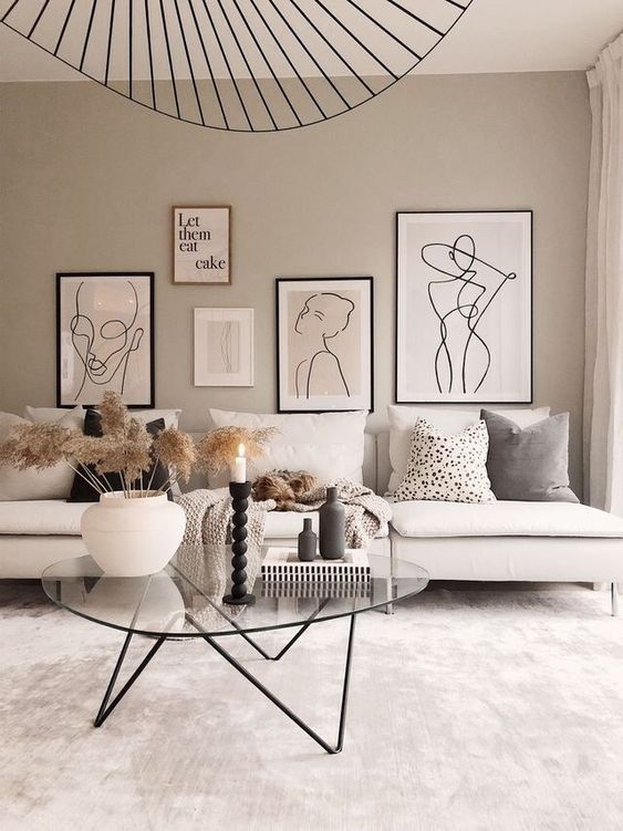 a neutral living room with a gallery wall, touches of black and a neutral sofa plus a glass table on metal legs