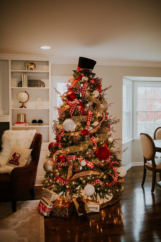 a decorated Christmas tree with lights, burlap and plaid ribbons, oversized red, gold and white ornaments abd a hat on top