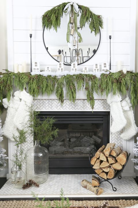 a lush evergreen garland on the mantel, mirror and white stockings hanging down from the mantel