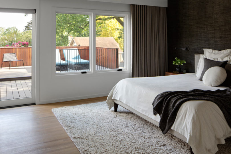 The bedroom is done with a black wall, a monochromatic bed and textiles, there's an entrance to a terrace