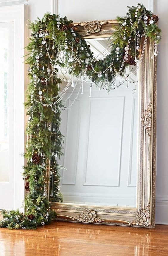 a lush evergreen garland with pinecones and crystals plus bead covers the large mirror bringing a strong Christmas feel to the space