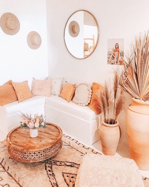 A neutral and warm toned boho living room with warm touches, rugs, a table and a terra cotta pot plus pampas grass