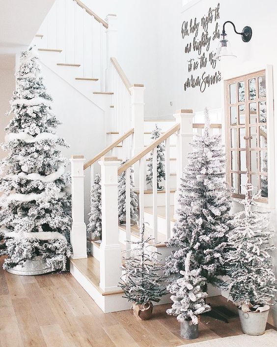 a winter wonderland entryway with multiple flocked trees with some white decor looks very dreamy