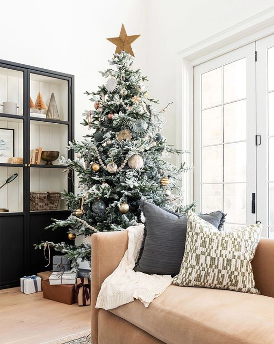 a flocked Christmas tree with sheer, gold and black ornaments including oversized ones and a star topper