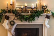 13 a lush greenery garland and neutral stockings hanging down plus pillar candles in wooden candleholders for elegant styling