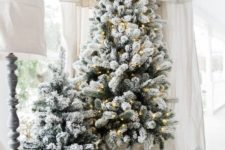14 flocked Christmas trees in buckets, one of them is decorated with lights look very nice a neutral farmhouse space