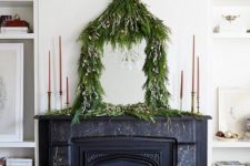 15 a lush greenery garland with mini ornaments covering a mirror on the mantel adds a quirky holidya touch to the space