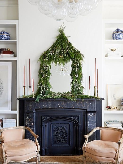 a lush greenery garland with mini ornaments covering a mirror on the mantel adds a quirky holidya touch to the space