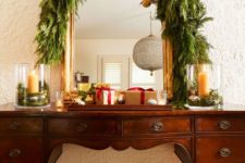 18 a vintage buffet covered with a lush greenery garland, with gold ornaments on red ribbons plus gift boxes looks very chic